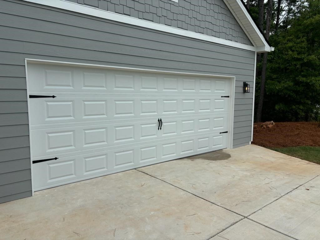 A white garage door with black hinges on a concrete driveway