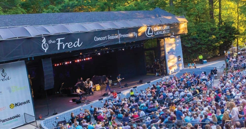 A large crowd of people are sitting in front of a stage at a concert in Peachtree City .