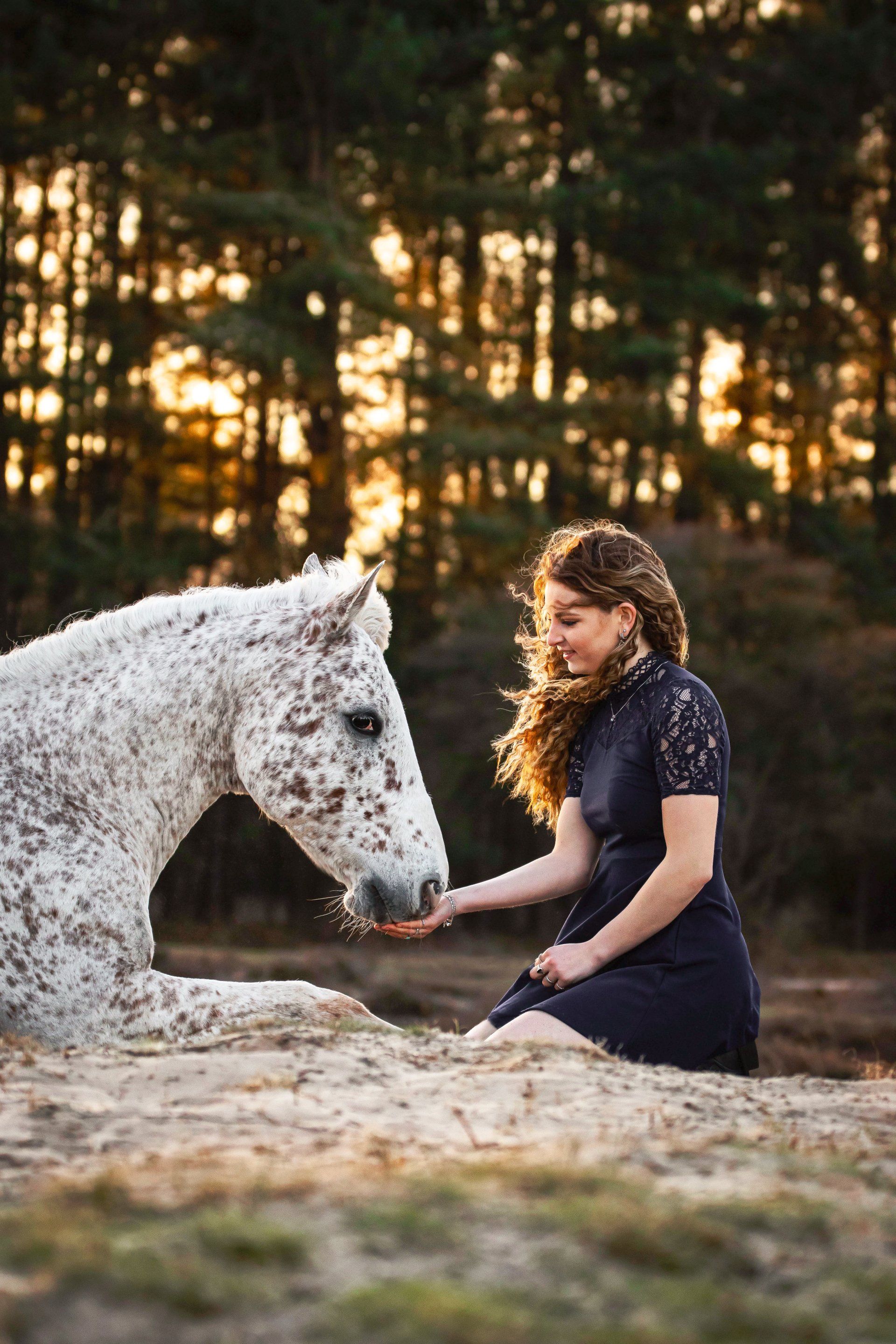 Een vrouw knielt neer naast een gevlekt paard.