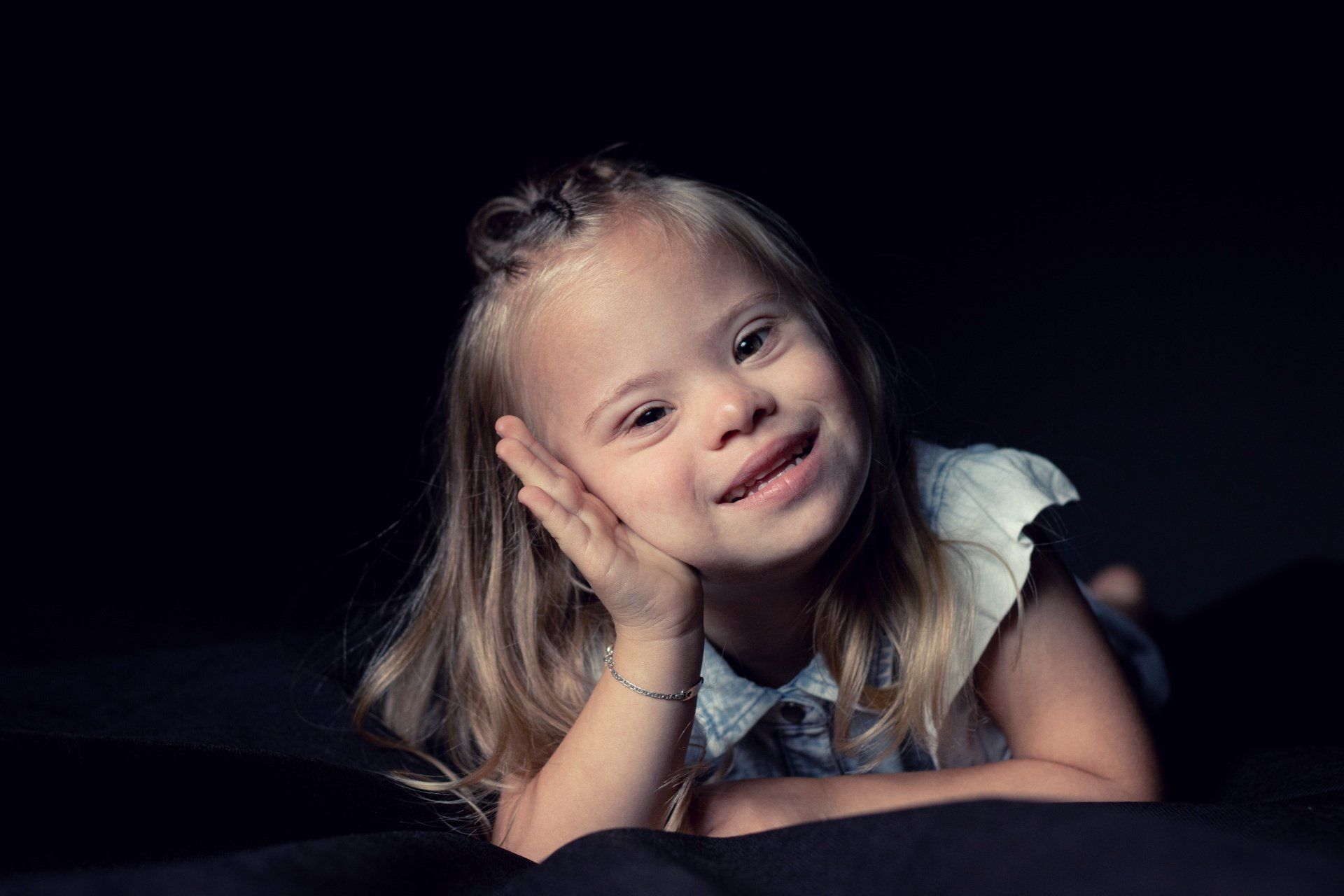 Een klein meisje met het syndroom van Down ligt op een bed en glimlacht.