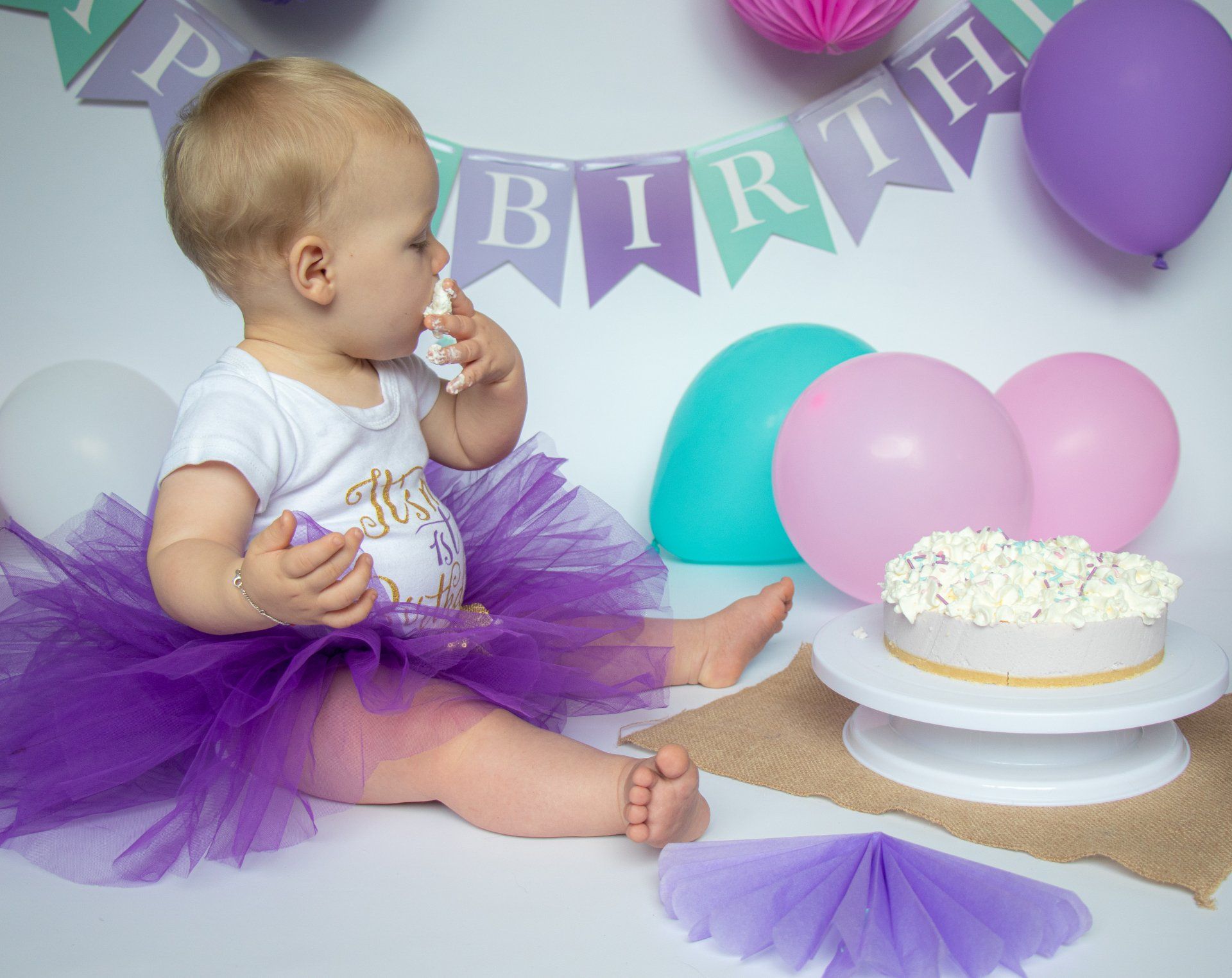 Een baby in een paarse tutu zit voor een verjaardagstaart.