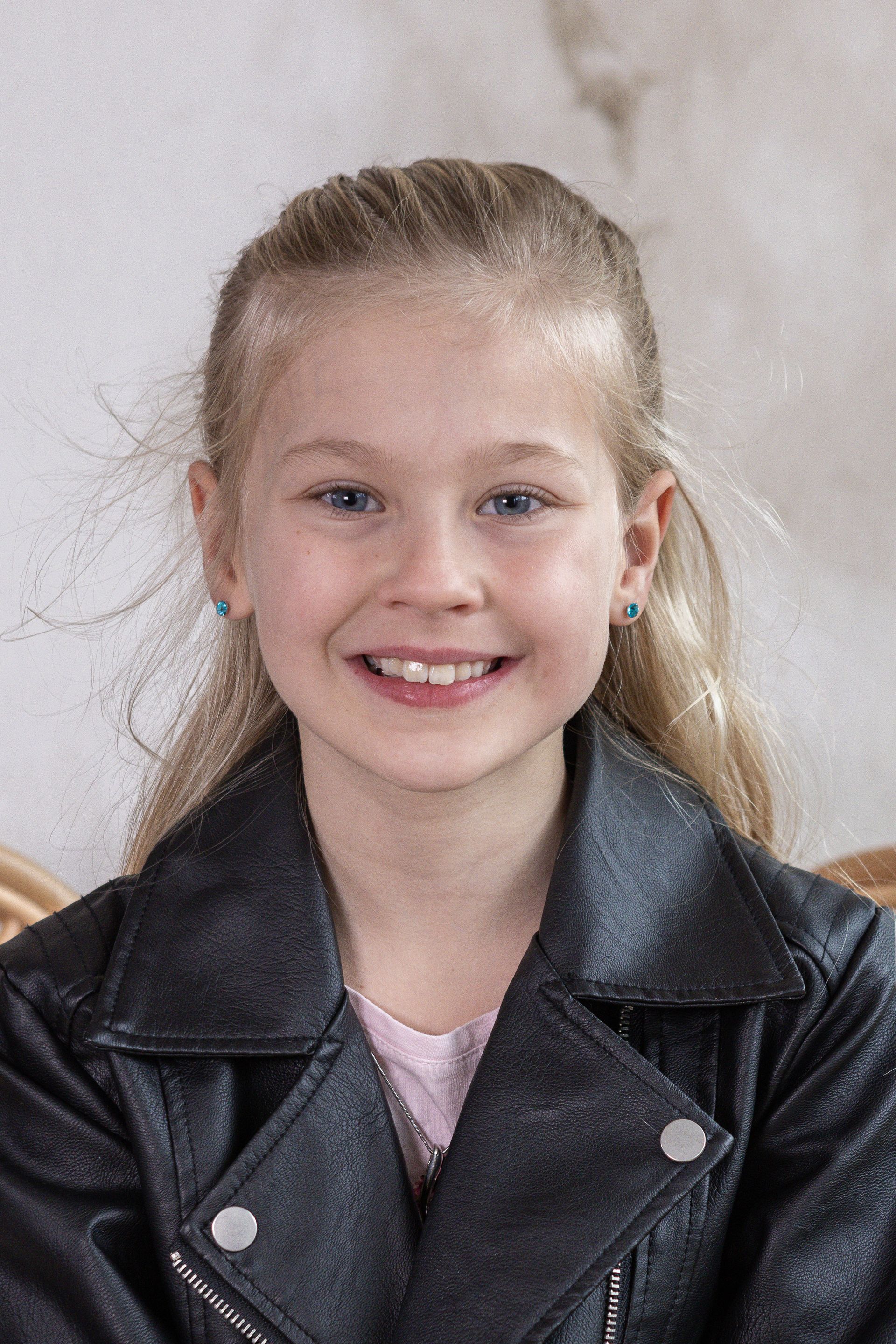 Een jong meisje dat een zwart leren jasje draagt, lacht naar de camera.