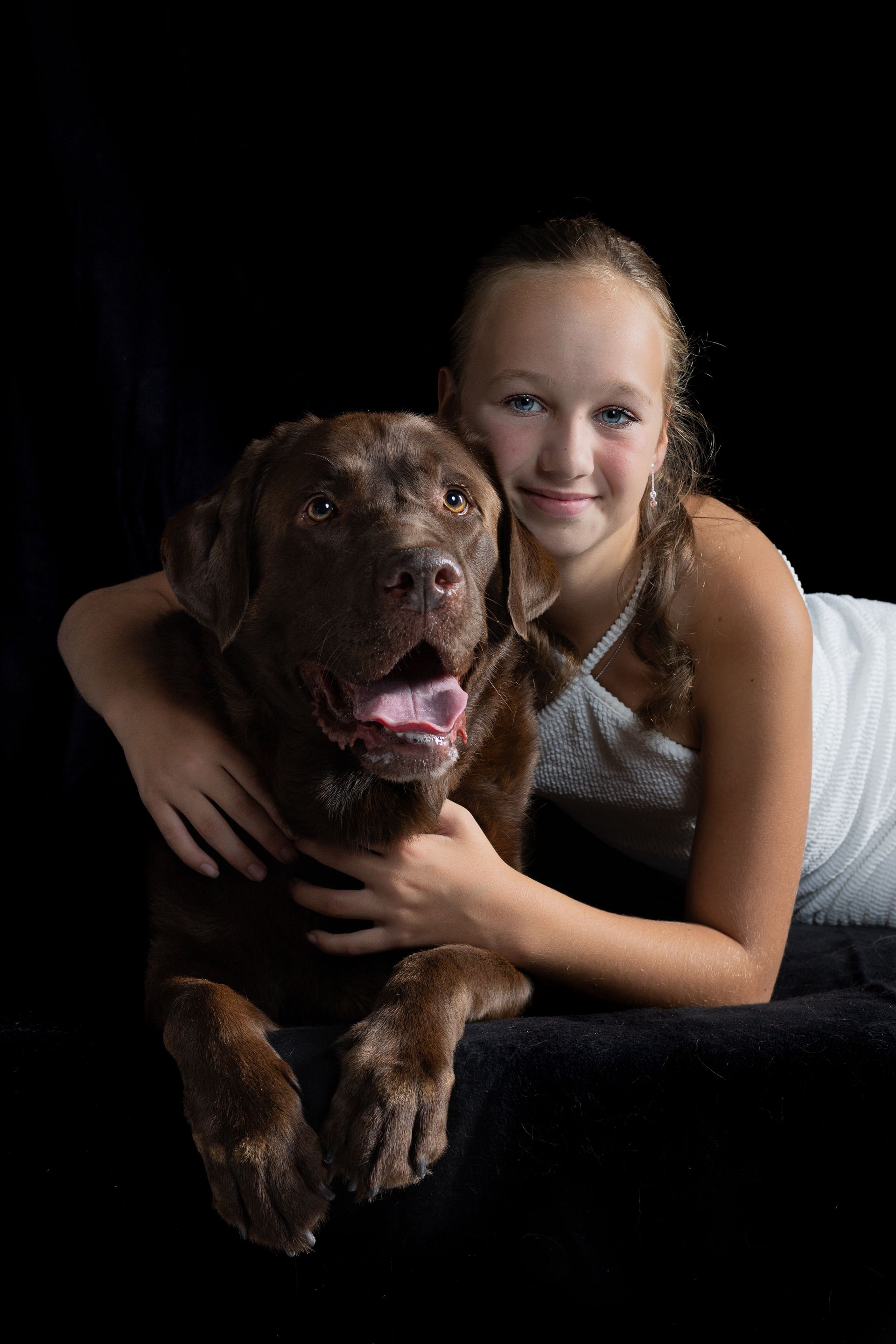 Een jong meisje ligt op de grond en houdt een bruine hond vast.