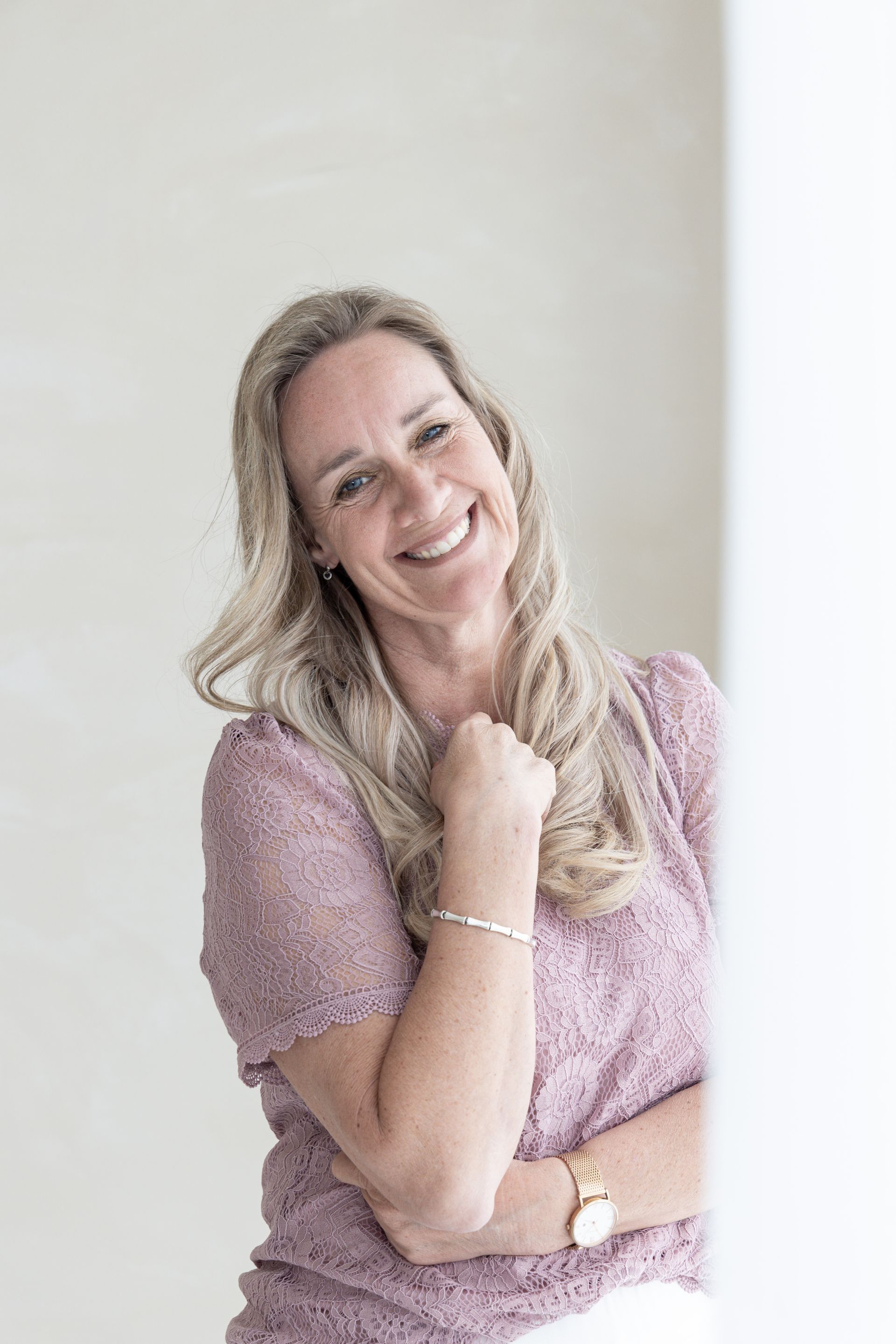 Een vrouw zit aan een tafel, houdt een camera vast en glimlacht.