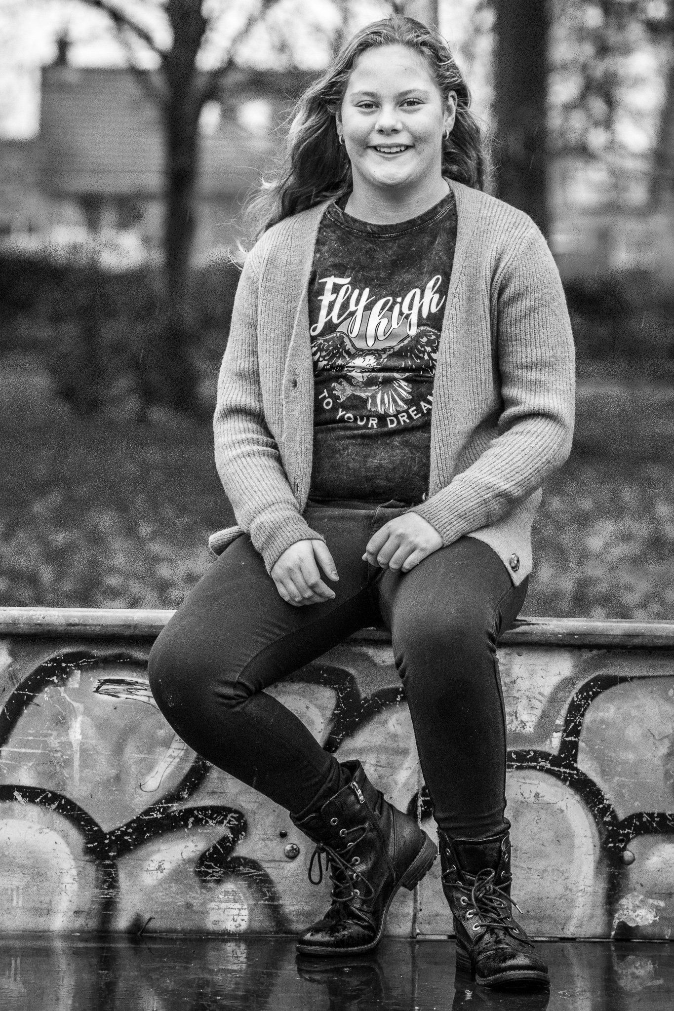 Een zwart-witfoto van een jong meisje dat op een muur zit.