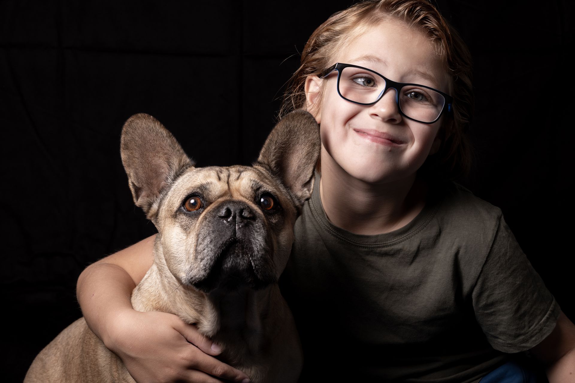 Een klein meisje met een bril houdt een Franse bulldog vast.