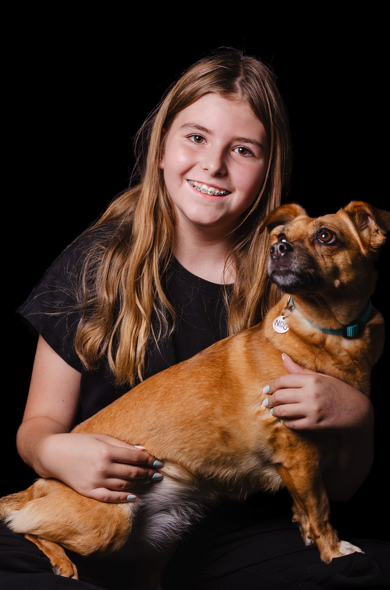 Een jong meisje houdt een bruine hond in haar armen.