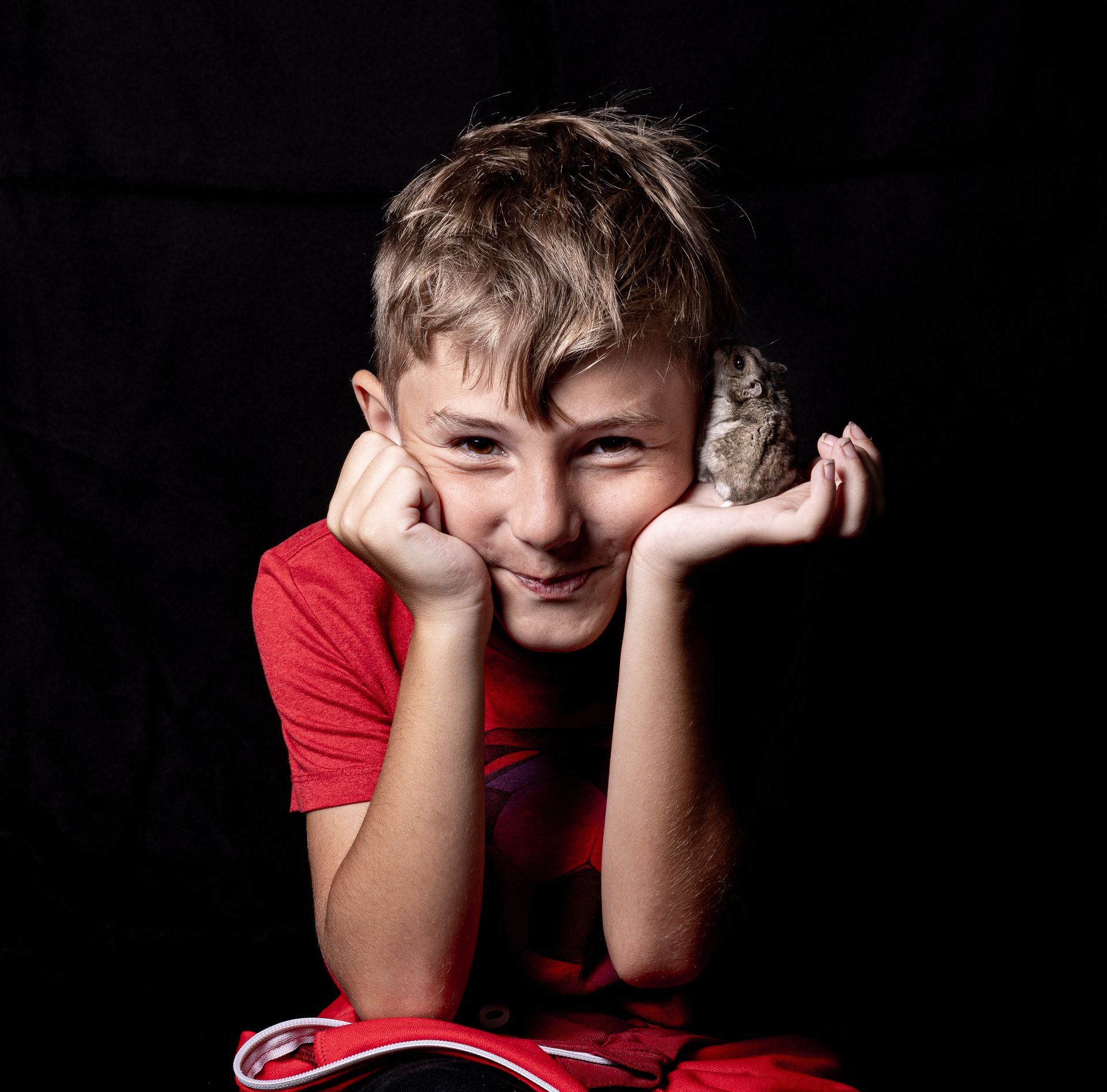 Een jonge jongen houdt een kleine hamster in zijn handen. Dierenfotograaf