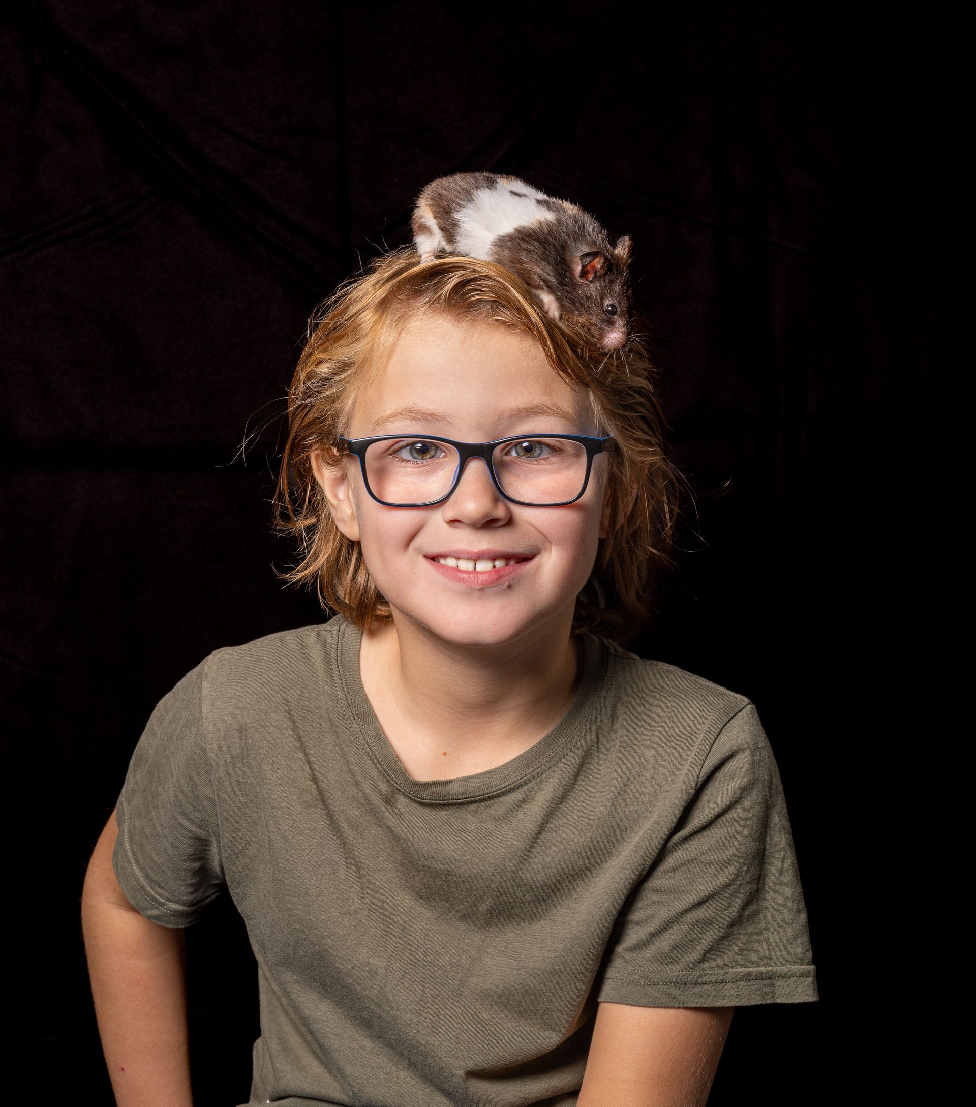 Een jonge jongen met een bril en een rat op zijn hoofd.