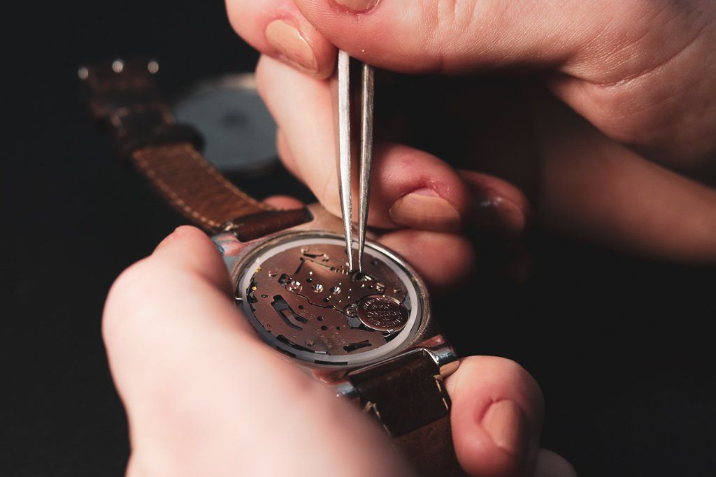 Een persoon repareert een horloge met een pincet.