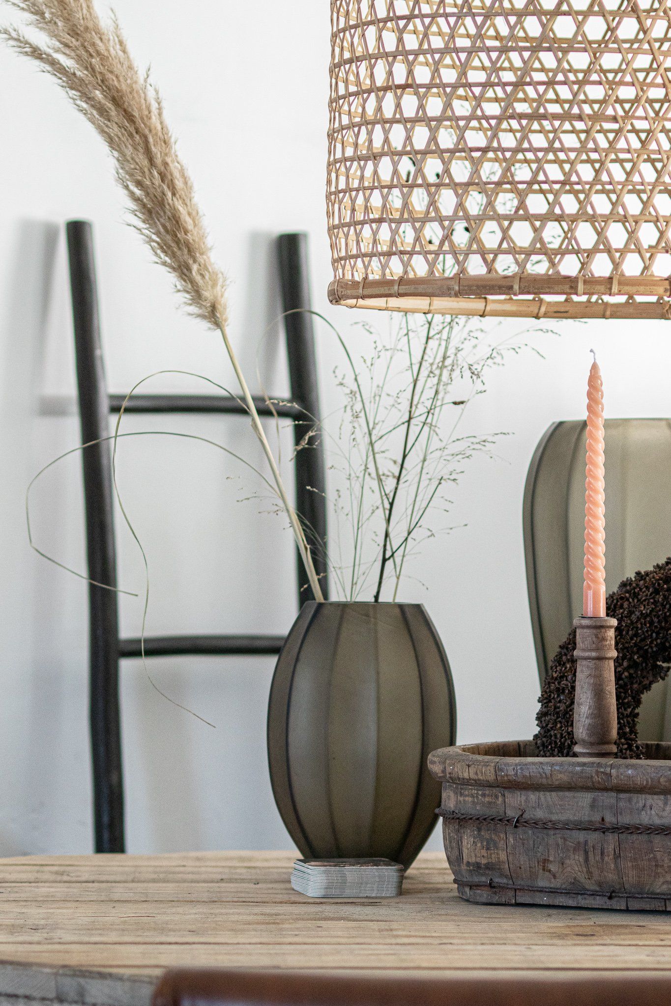 Op een houten tafel staat een vaas met bloemen erin, naast een lamp.