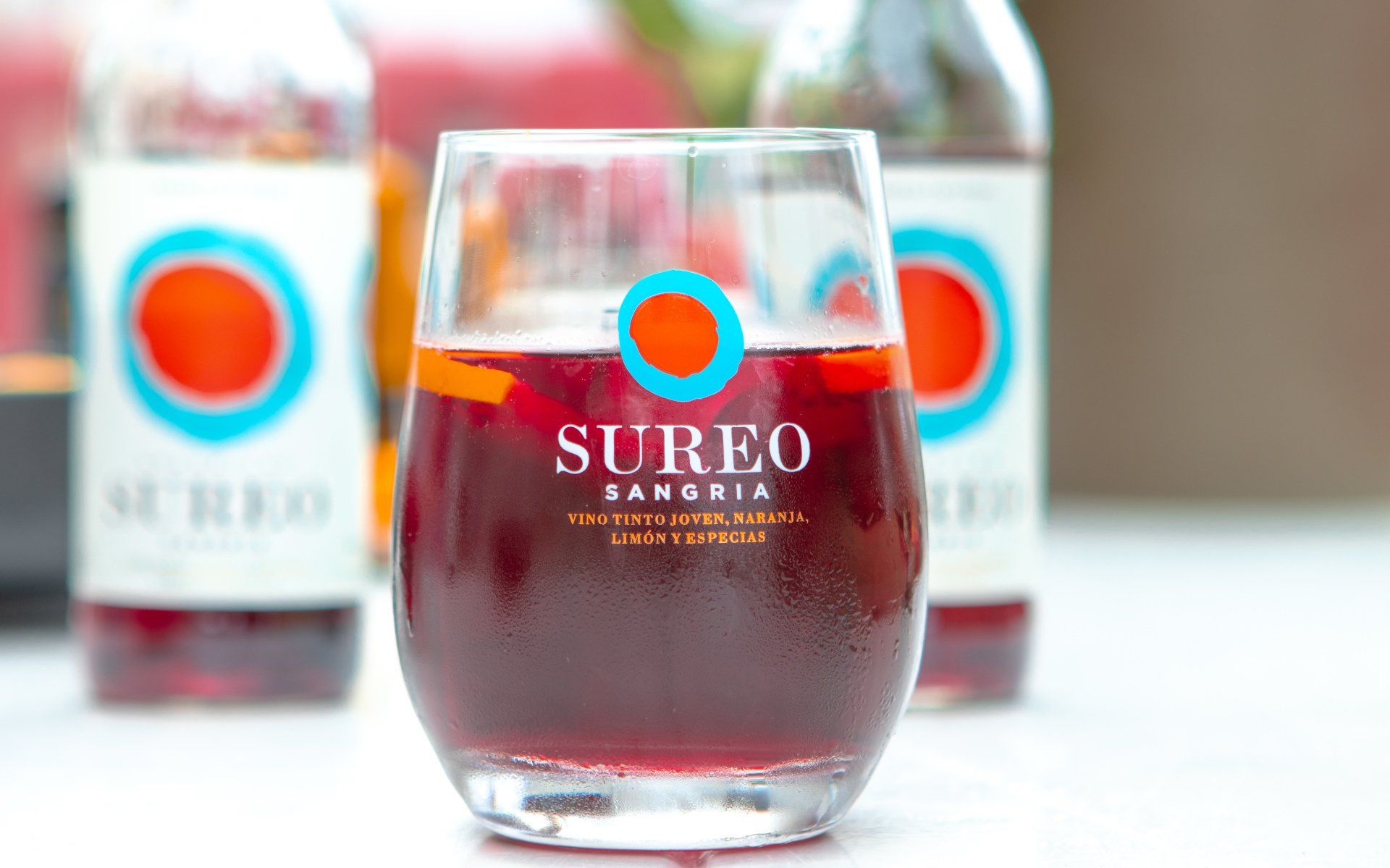 Op een tafel staat een glas wijn naast flessen wijn. Sureo