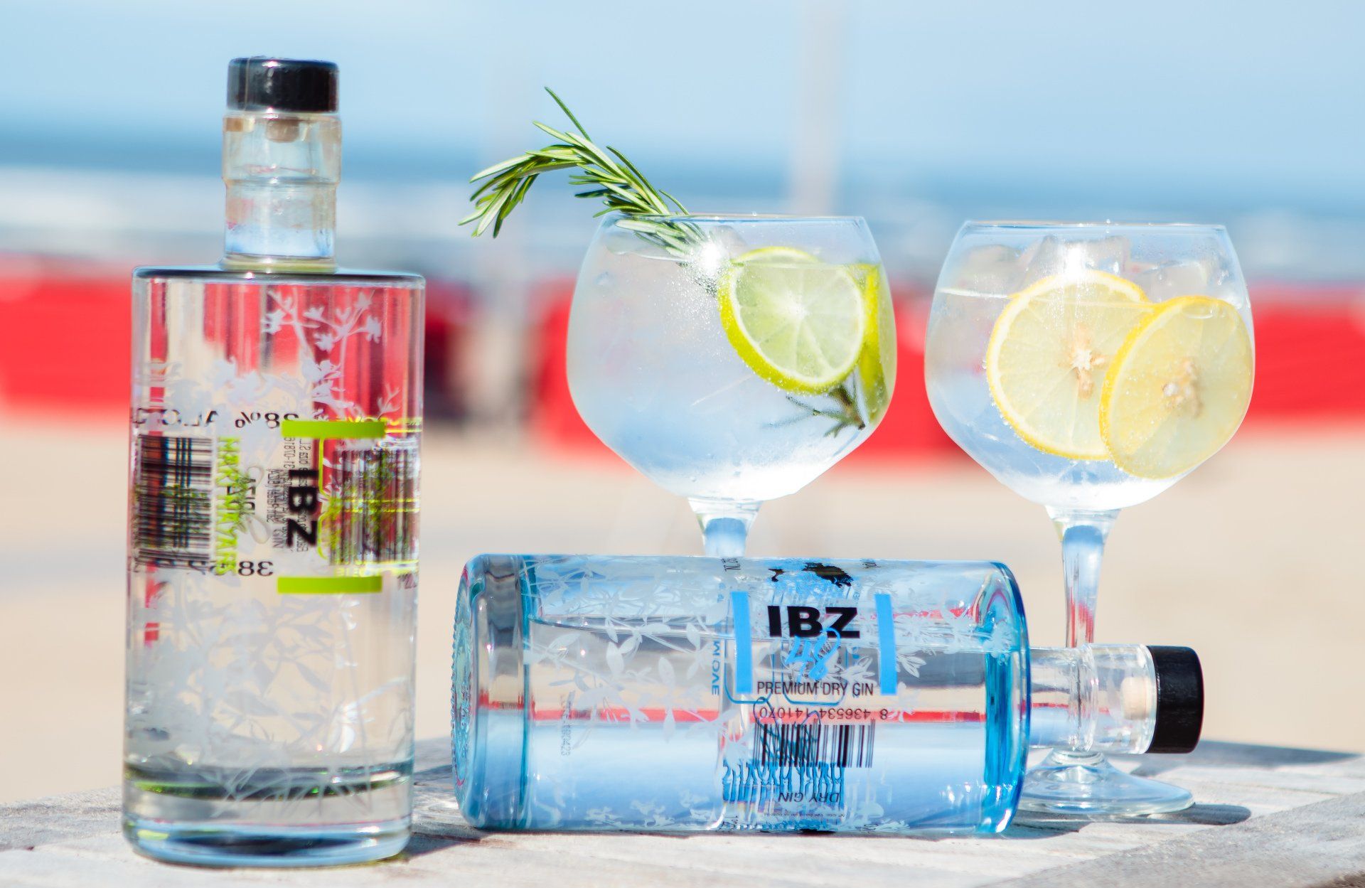 Twee flessen gin en twee glazen gin op een tafel op het strand.