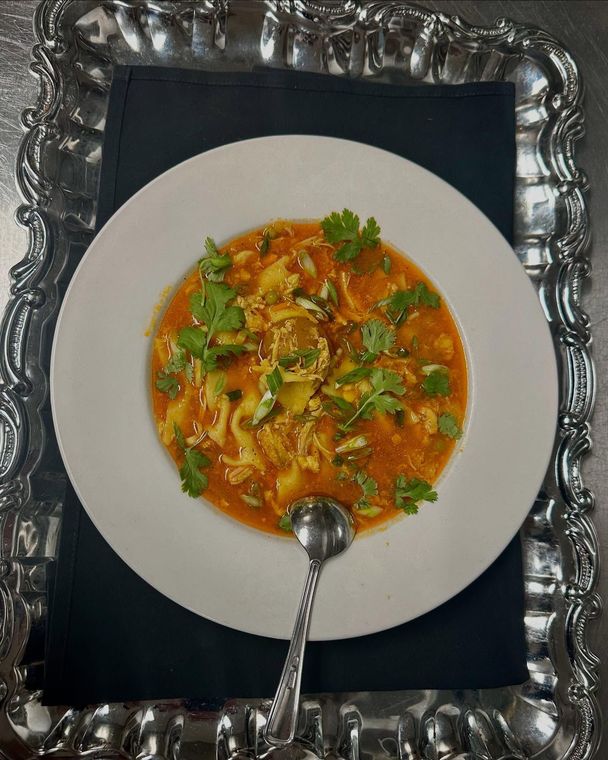 A bowl of soup with a spoon in it on a silver tray.