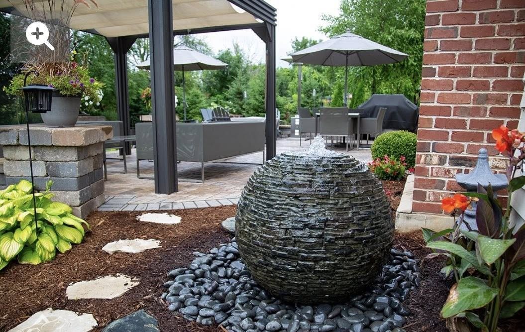 Water fountain in a landscaped backyard with a seating area under a pergola and patio furniture.