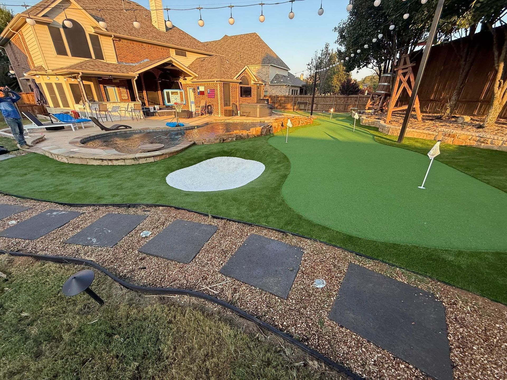 Backyard with putting green, sand trap, stepping stones, and house.