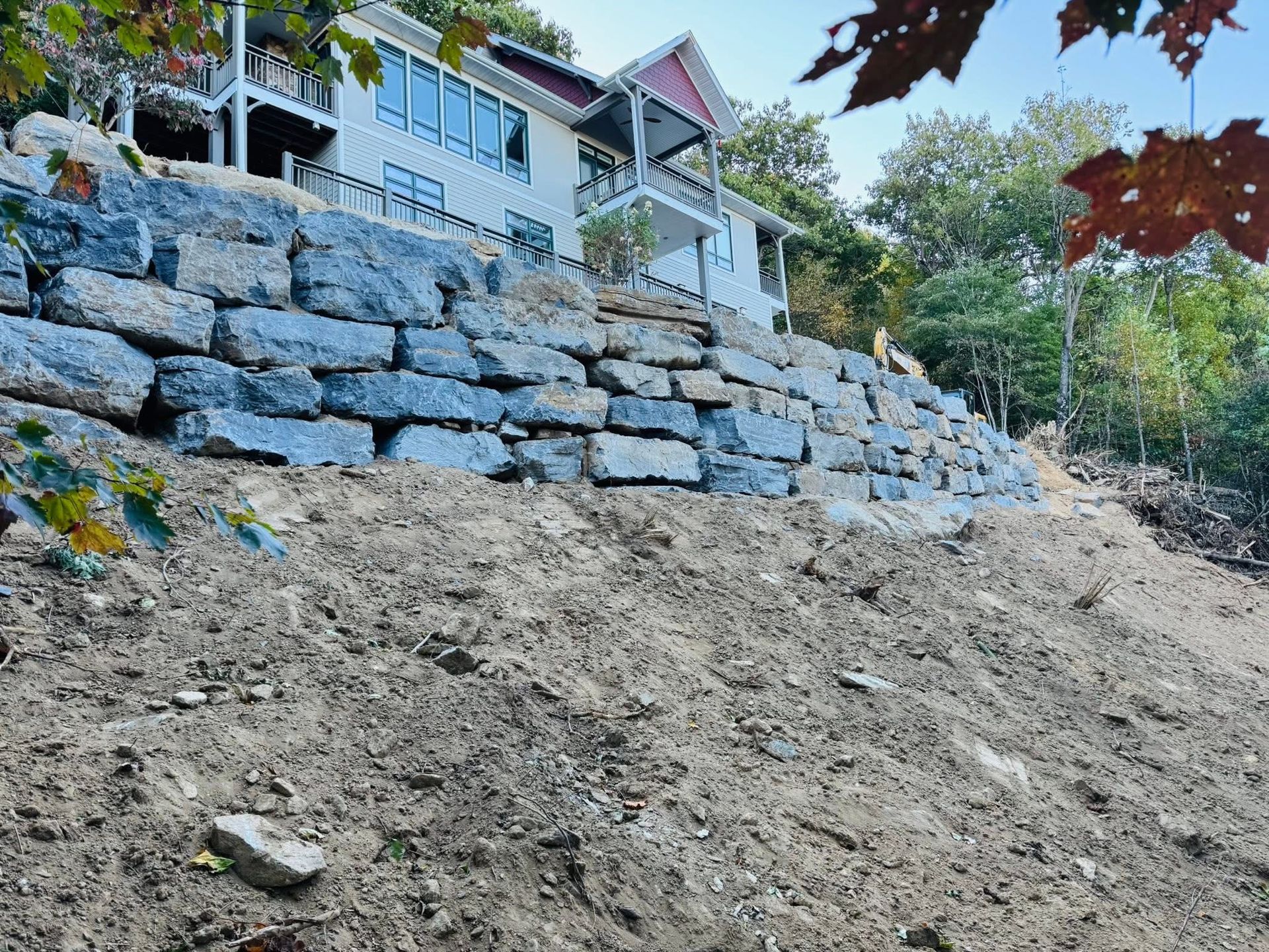 Stone retaining wall on a hillside with a house in the background. Brown dirt in the foreground.