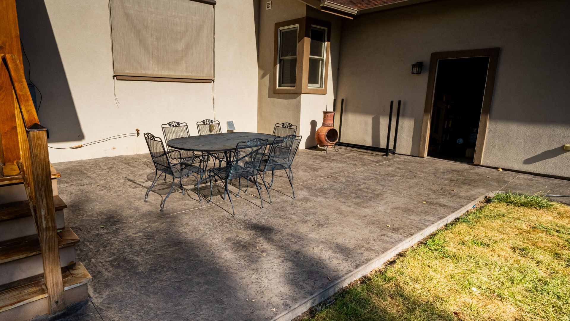 Patio with metal table and chairs on a concrete terrace beside a building, with a patch of grass nearby