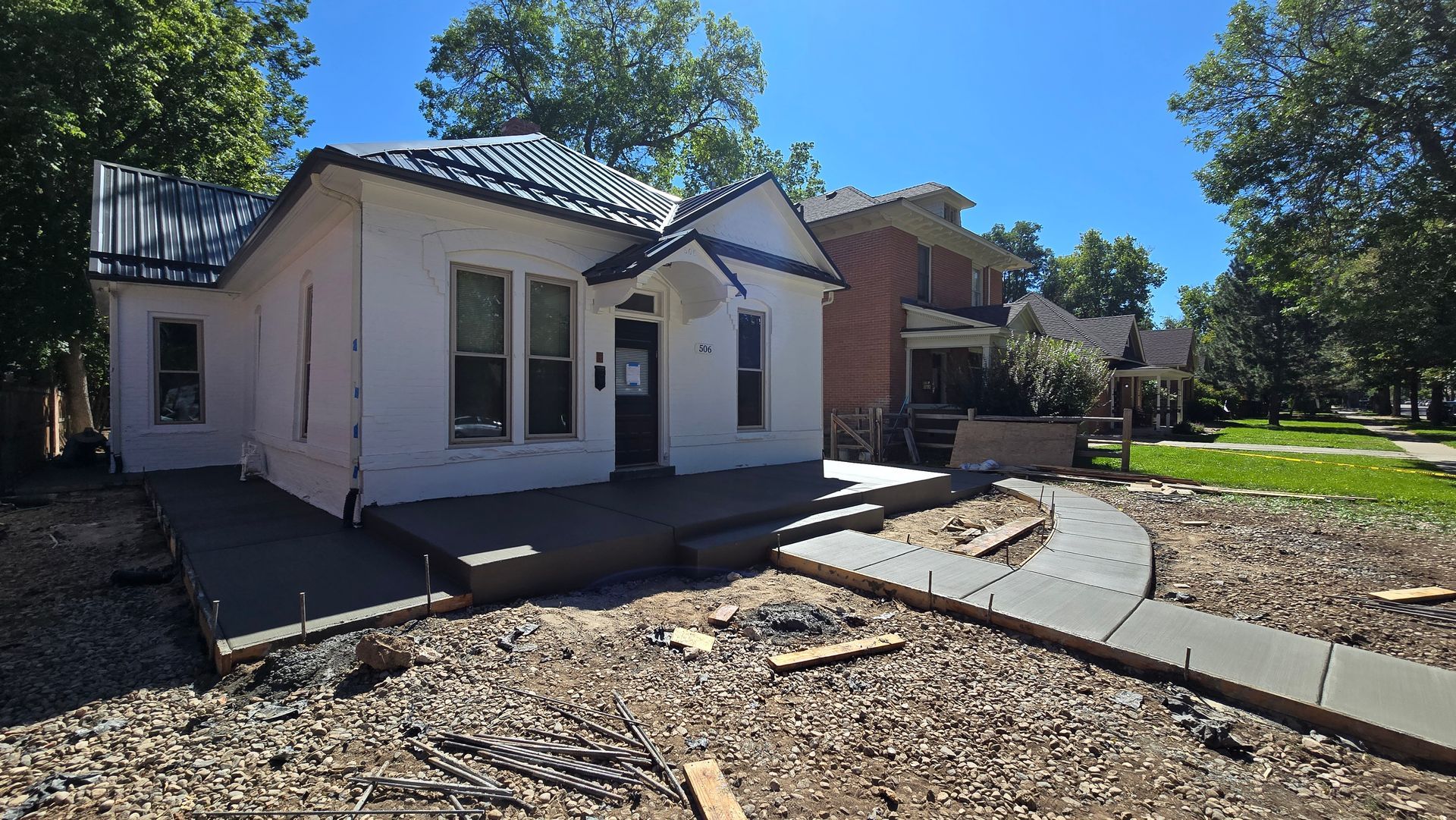 Small white house with a blue roof, front walkway, and landscaped yard under a clear blue sky.
