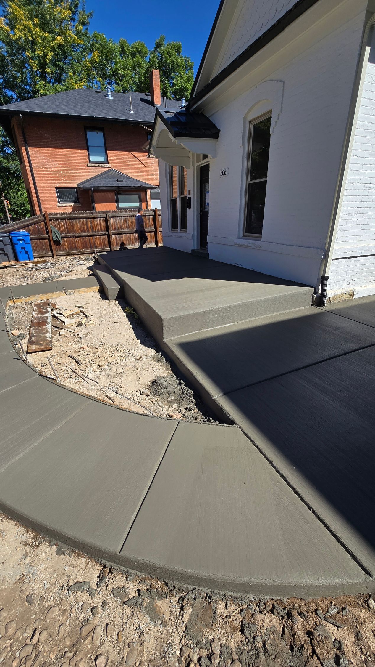 Concrete walkway beside a white house, curving through a backyard construction area with brick and gravel.
