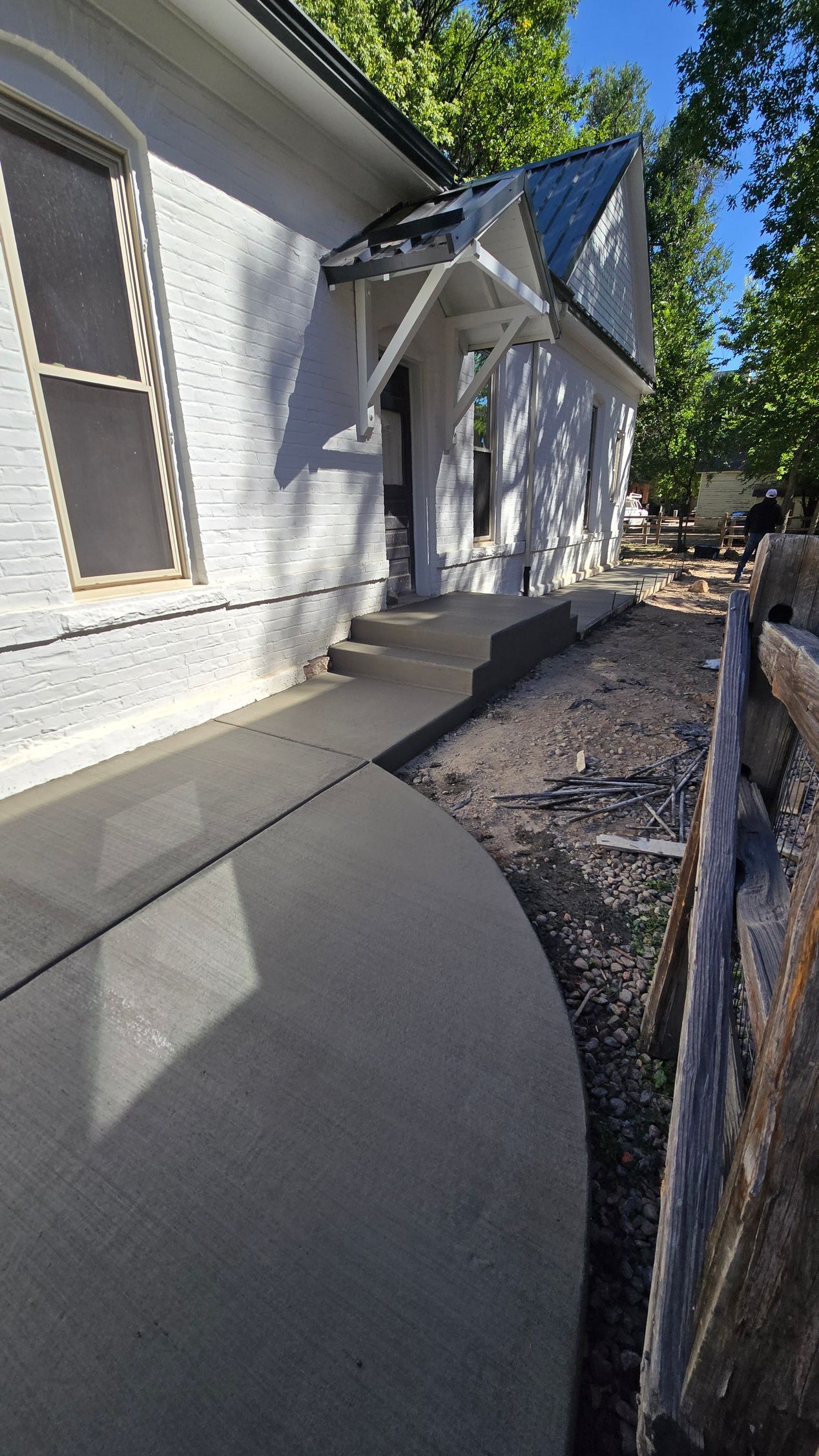 White house exterior with a curved concrete walkway, gravel bed, and wooden fence along the side.