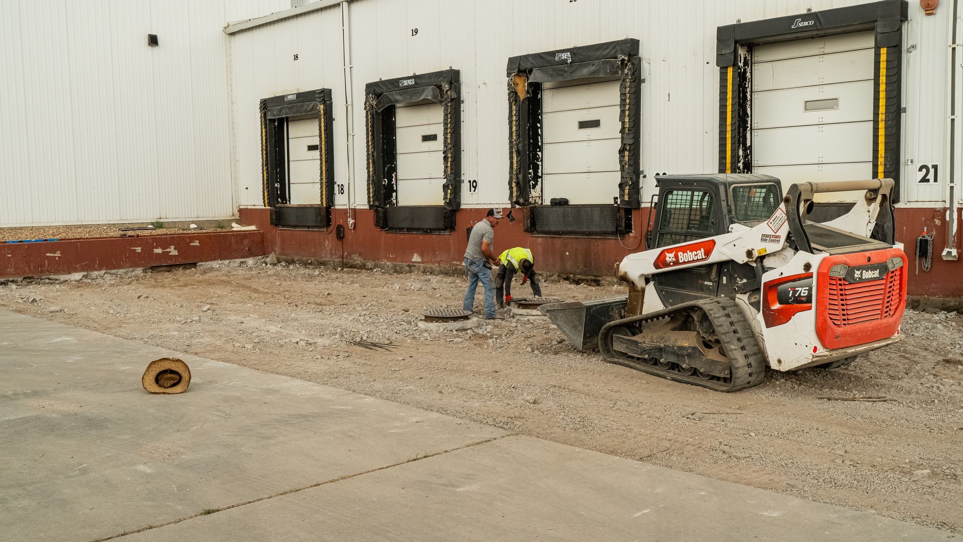 Worker using a skid steer clears rubble outside a warehouse loading dock.