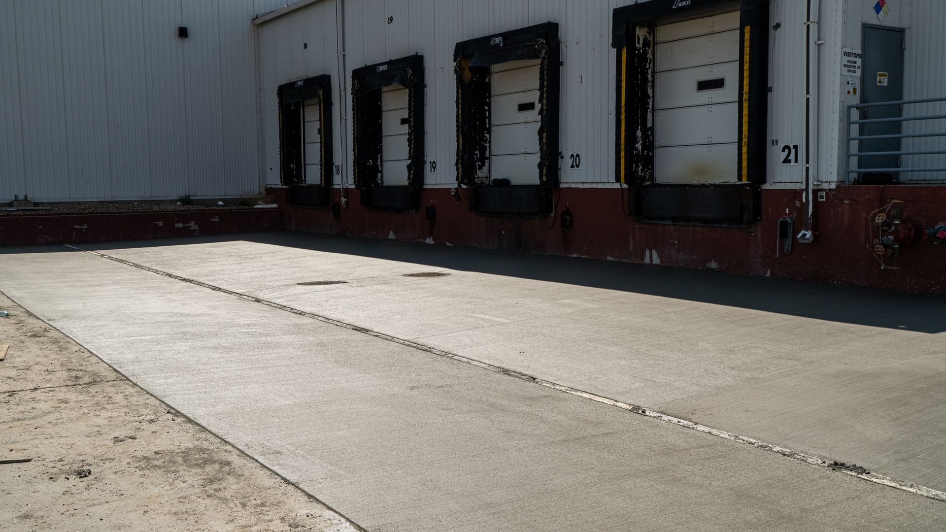 Warehouse loading dock with three truck bays beside a sunlit concrete lot