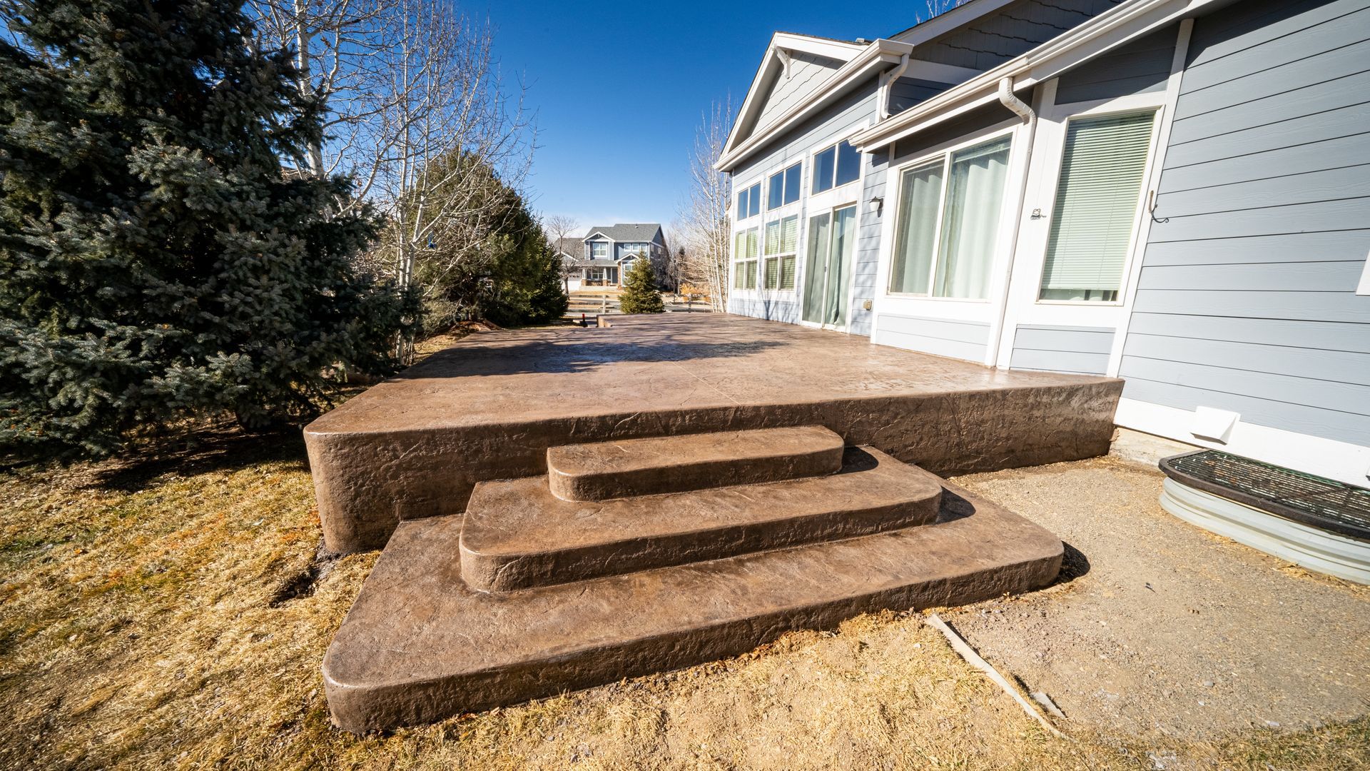 Concrete steps leading to a raised patio beside a light blue house on a sunny day