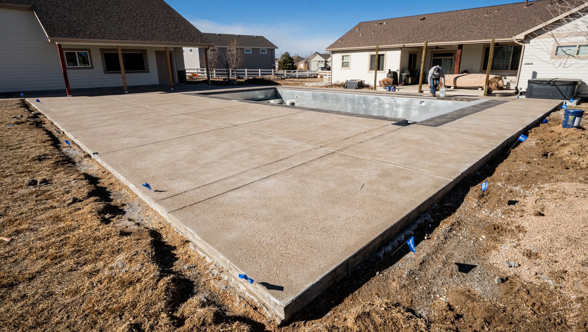Concrete patio foundation in a backyard under construction, surrounded by dirt and houses.