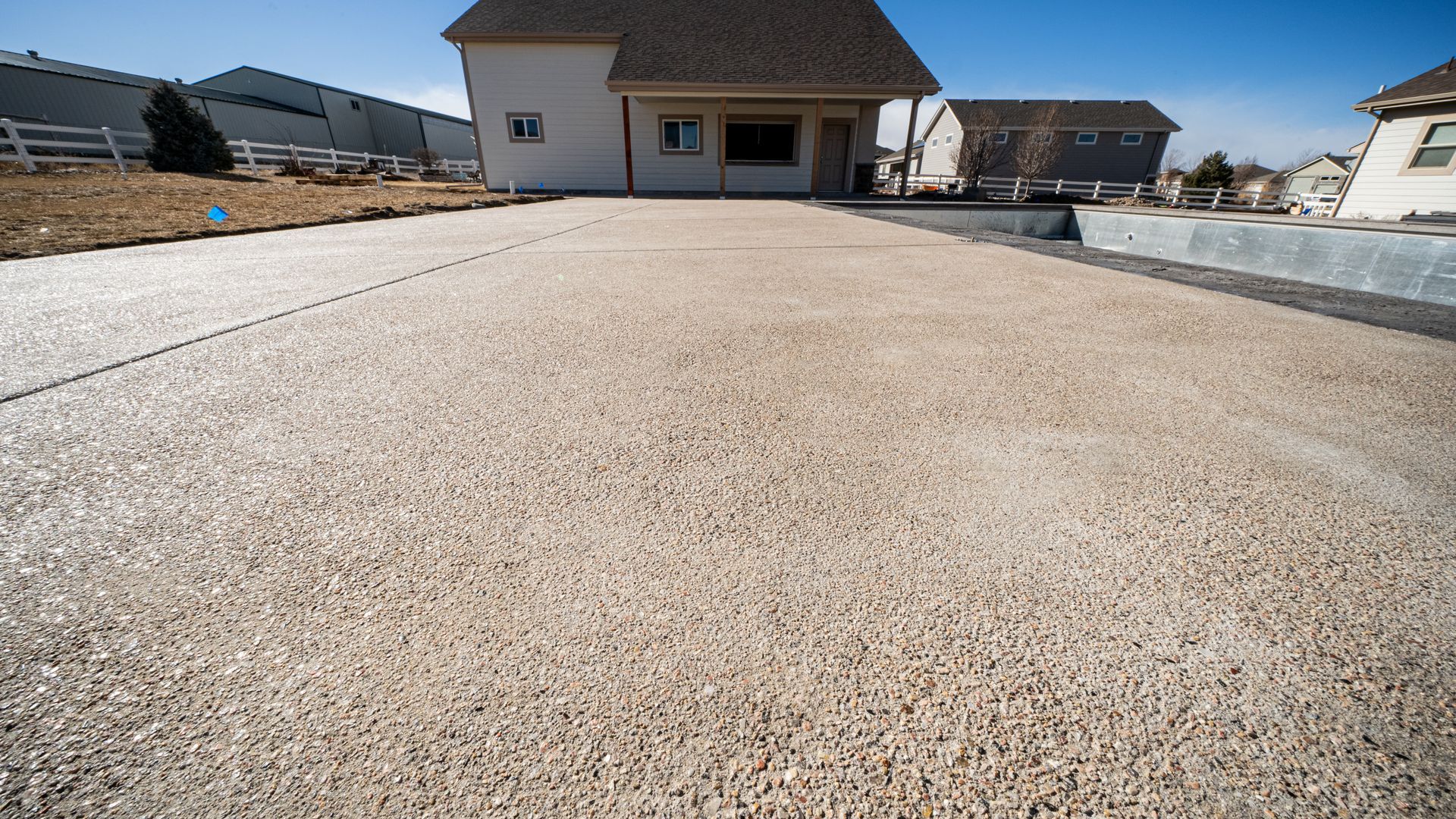 Wide gravel driveway leading to a suburban house under clear daylight, with homes on both sides.