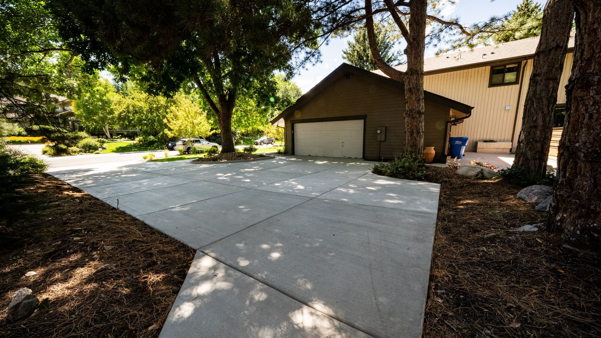Concrete driveway leading to a tan garage beside tall trees and a wooded yard