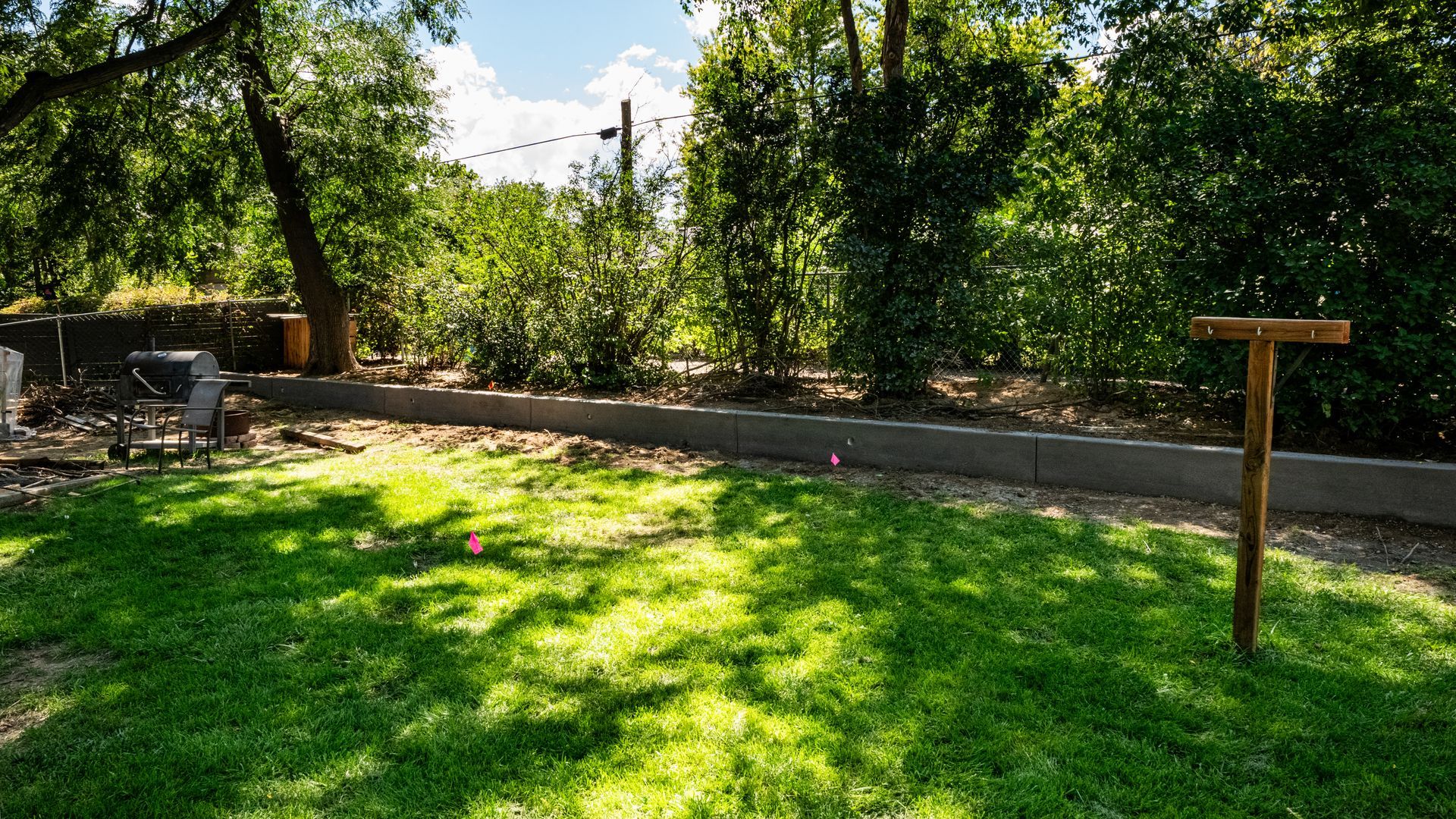 Sunny garden with green lawn, stone path, trees, and a wooden sign beside a fence
