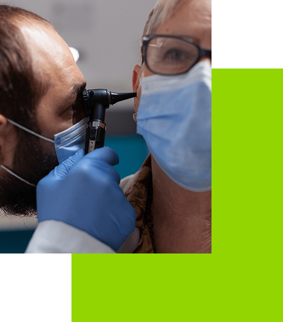 Un hombre que lleva una máscara se está haciendo examinar los oídos por un médico.