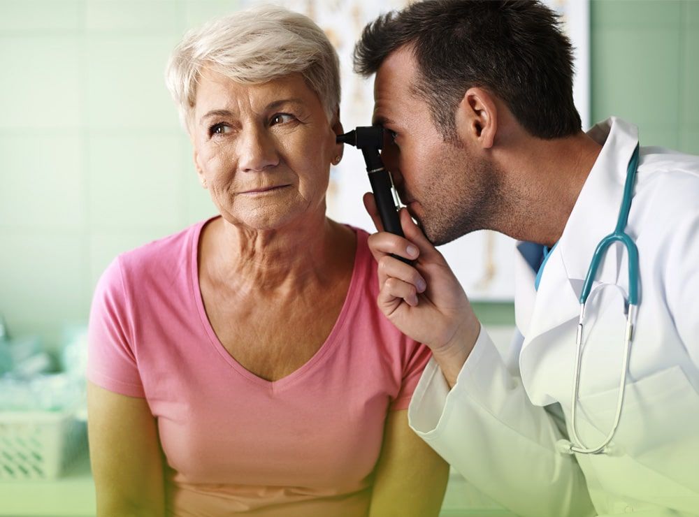 Un médico está examinando la oreja de una mujer mayor con un otoscopio.
