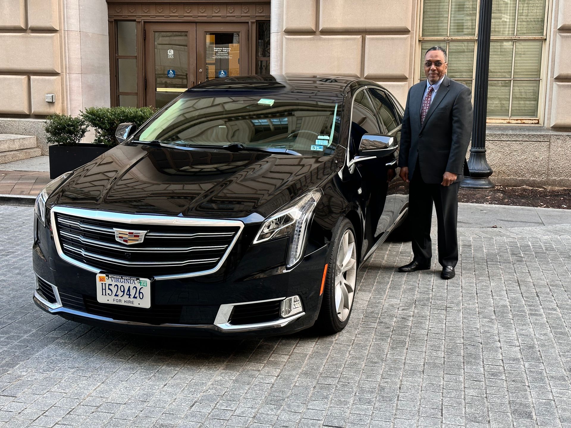 A man in a suit and tie is standing next to a black cadillac.