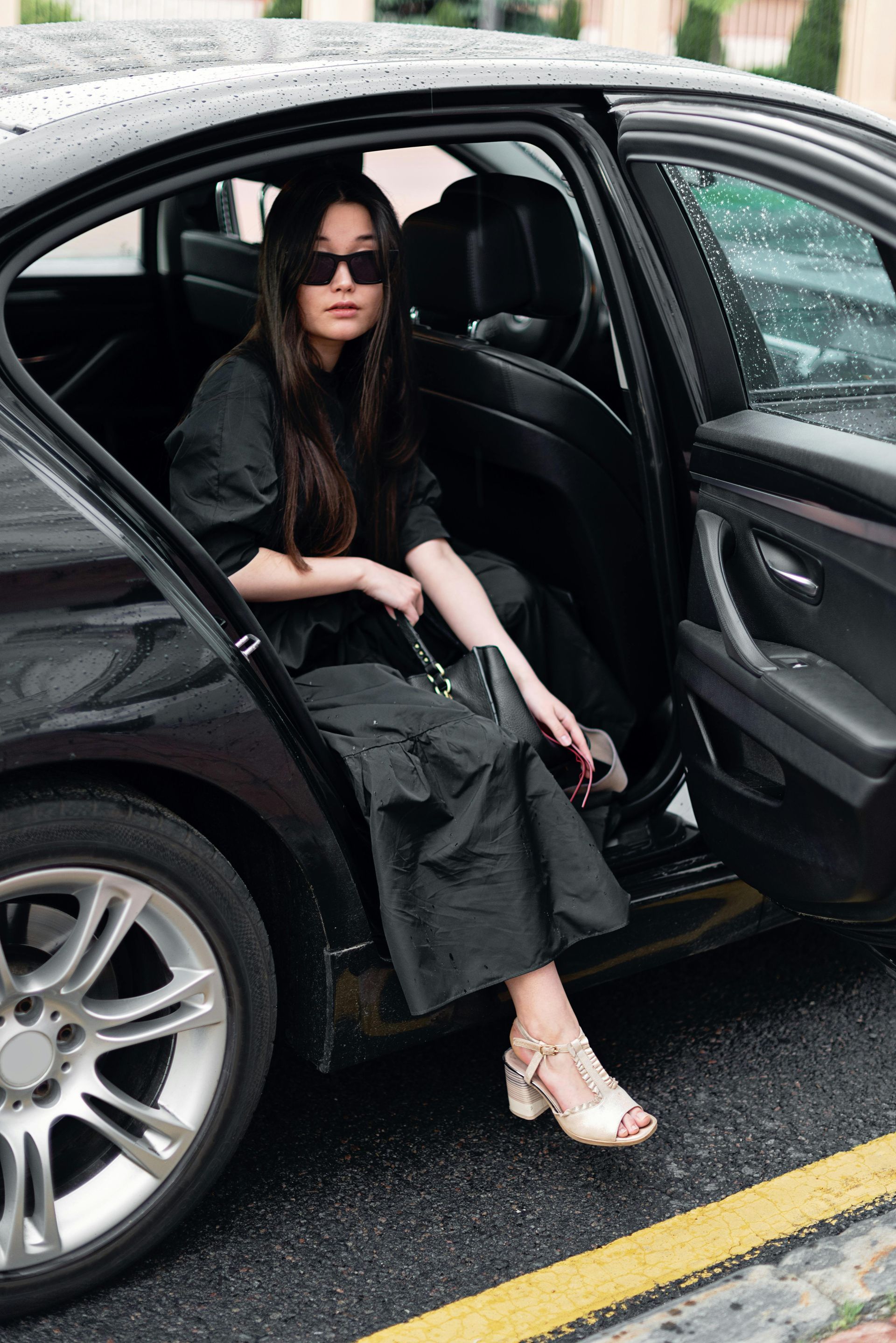 A woman is sitting in the back seat of a black car.