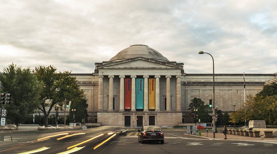 A car is driving down a street in front of a large building.