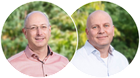 Two men in button-down shirts, one pink and one white, smiling in front of a blurry outdoor green background.