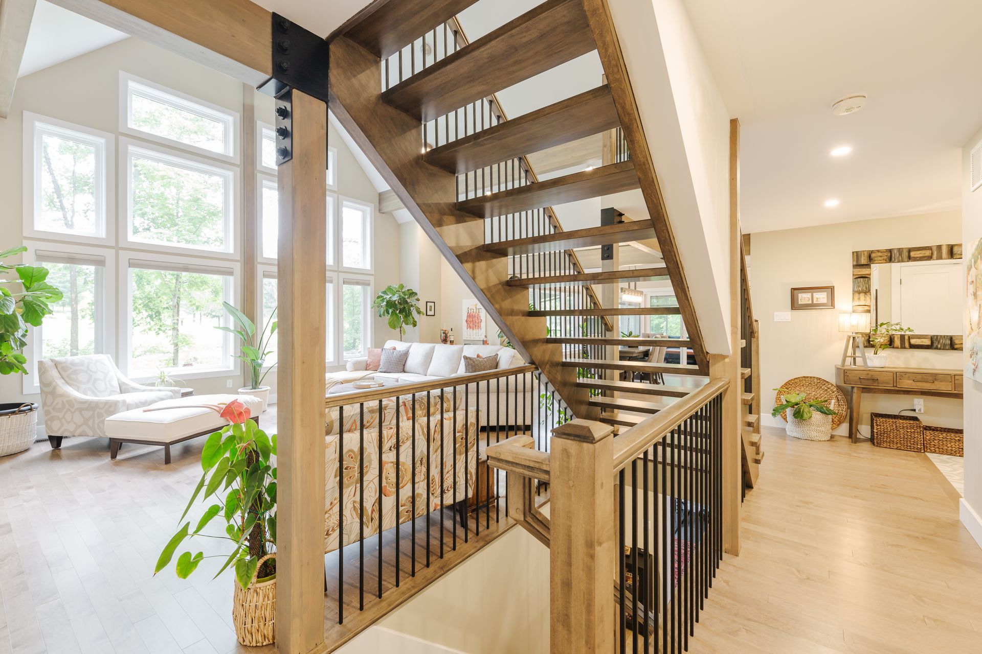 Staircase with wood steps and black railings, leading to a living area with large windows and neutral decor.