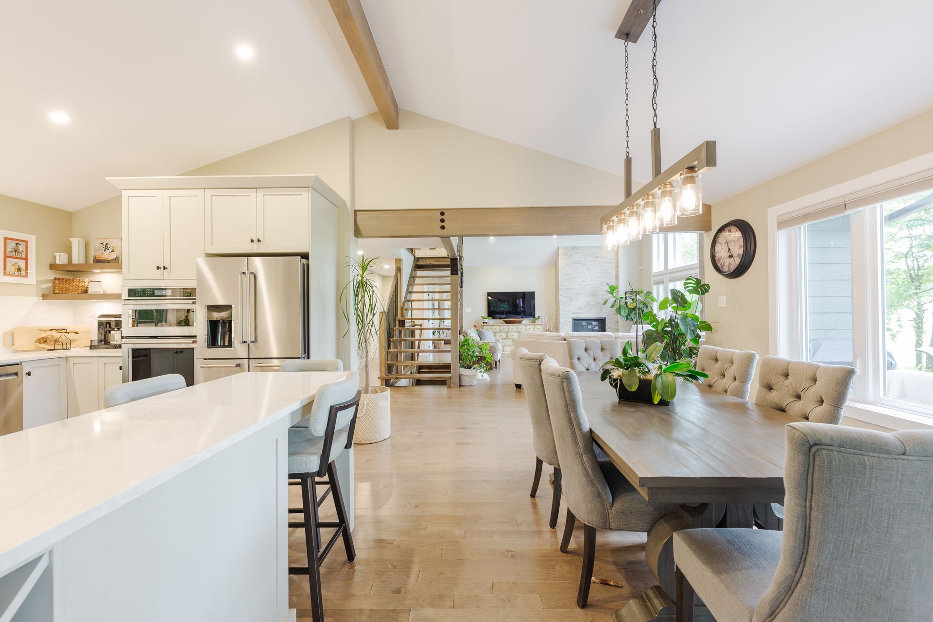 Open-concept kitchen with white cabinets, island seating, dining area, and living room with natural light.