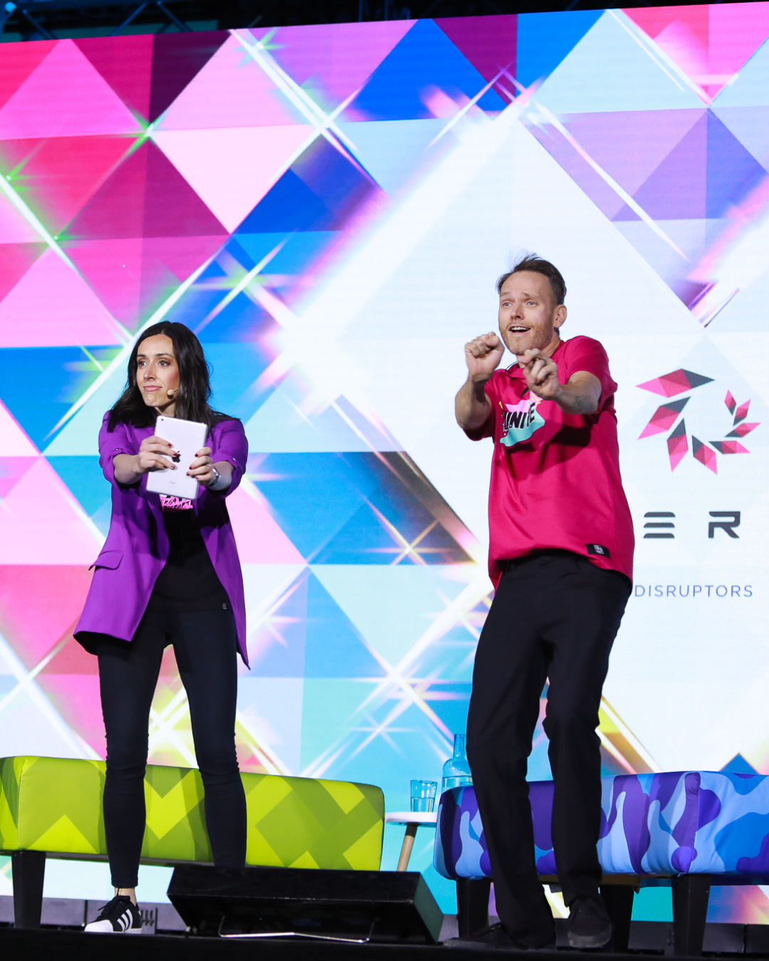 A man and a woman are standing on a stage in front of a large screen with the letter r on it