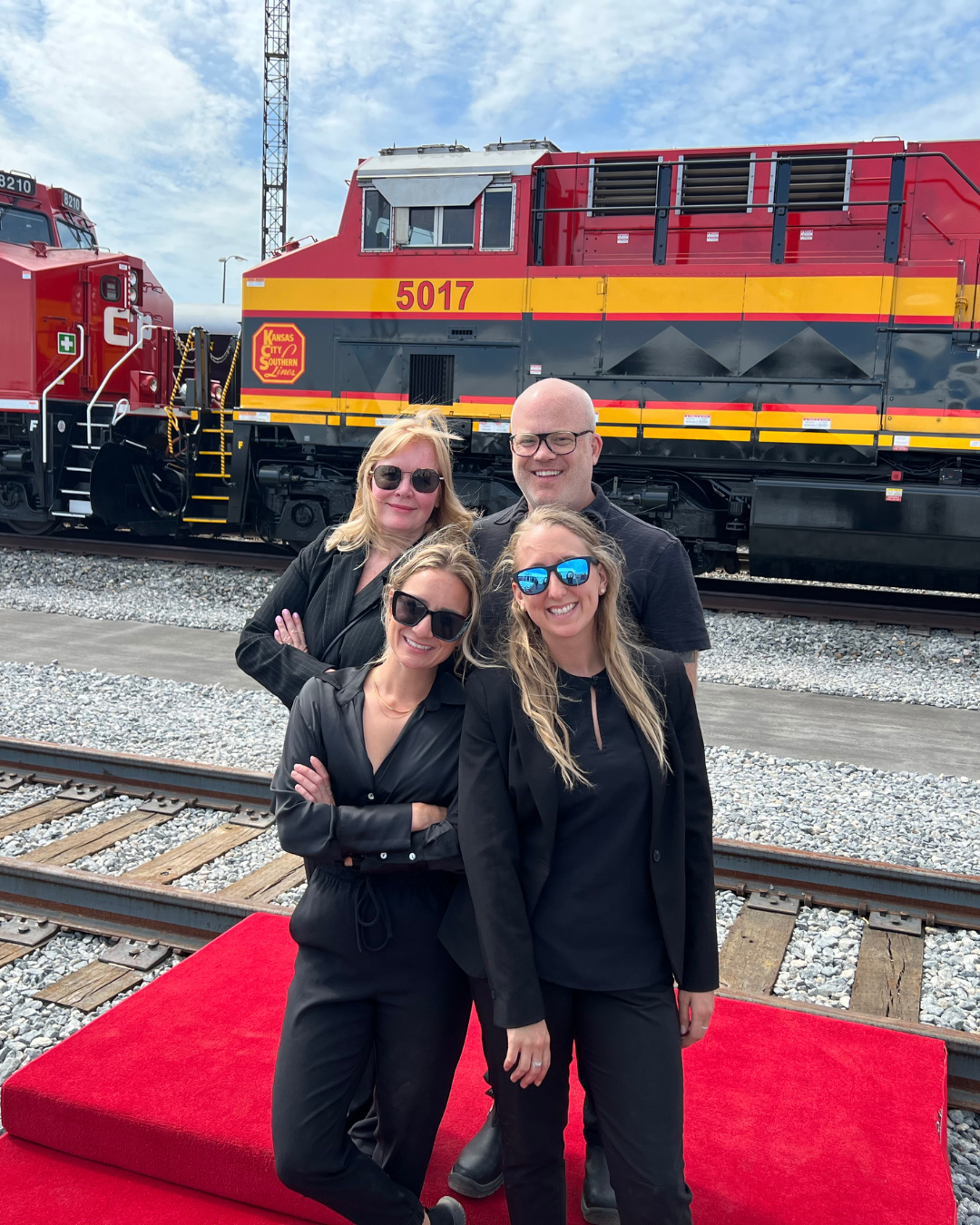 A group of people standing on a red carpet in front of a train.