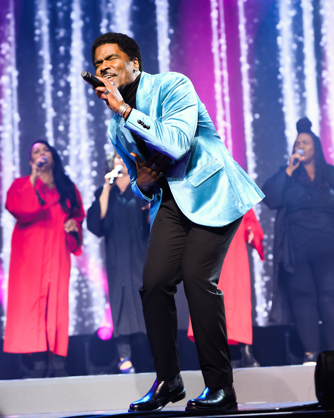 A man in a blue jacket is singing into a microphone on a stage.