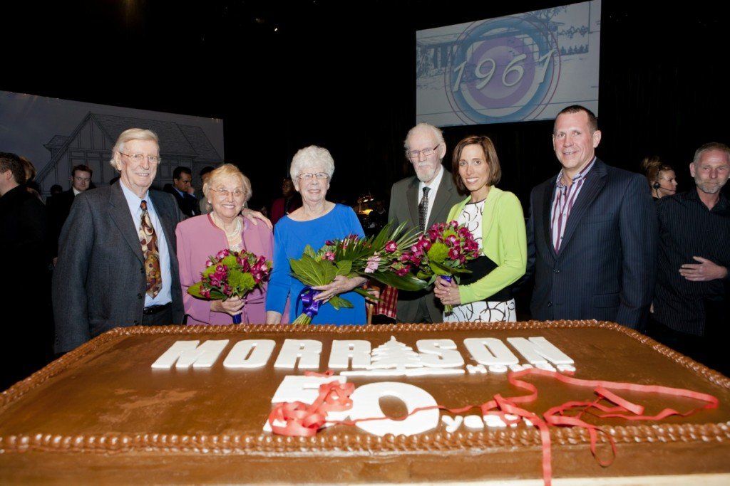 A group of people standing around a cake that says moraman 50 years