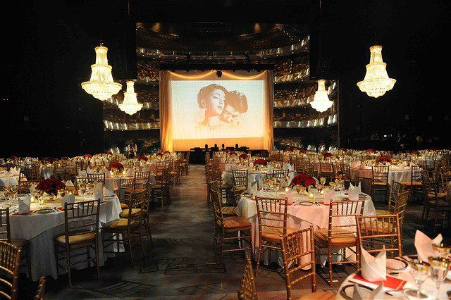 A large auditorium filled with tables and chairs and a large screen with a picture of a woman on it.