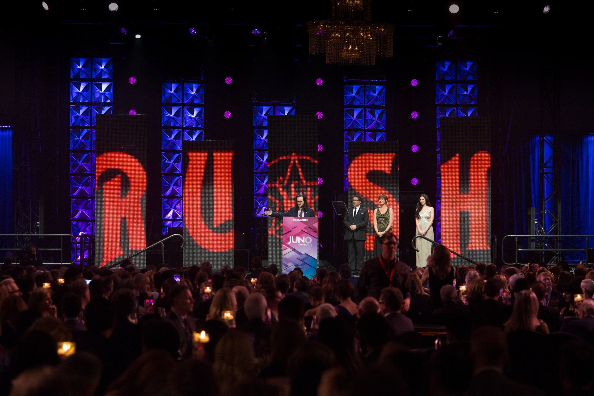 A crowd of people are sitting in front of a large screen that says rush