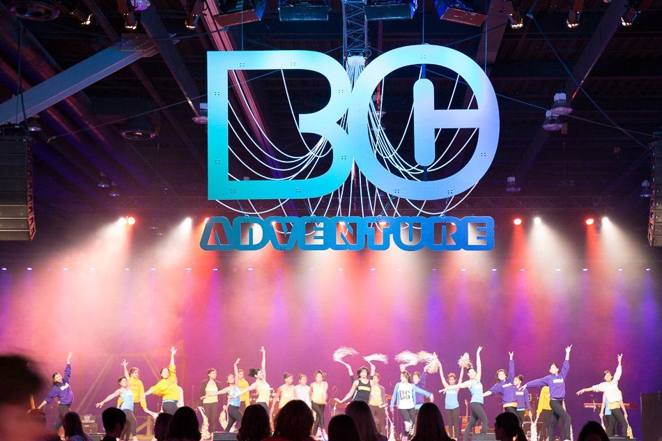 A group of people are dancing in front of a stage that says be adventure