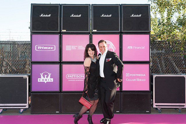 A man and a woman are standing in front of a wall of speakers.
