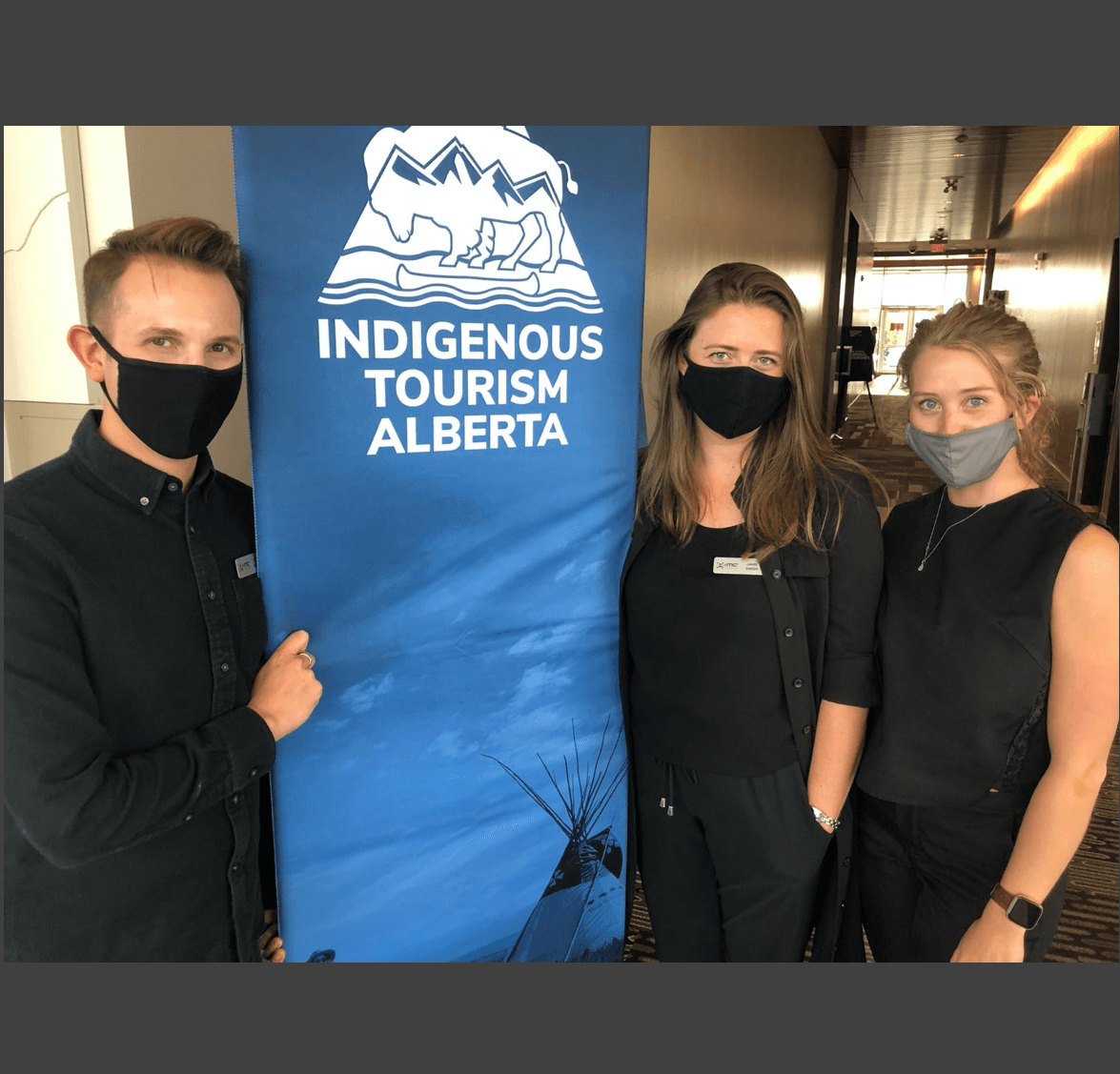 Three people wearing face masks stand in front of a sign that says indigenous tourism alberta