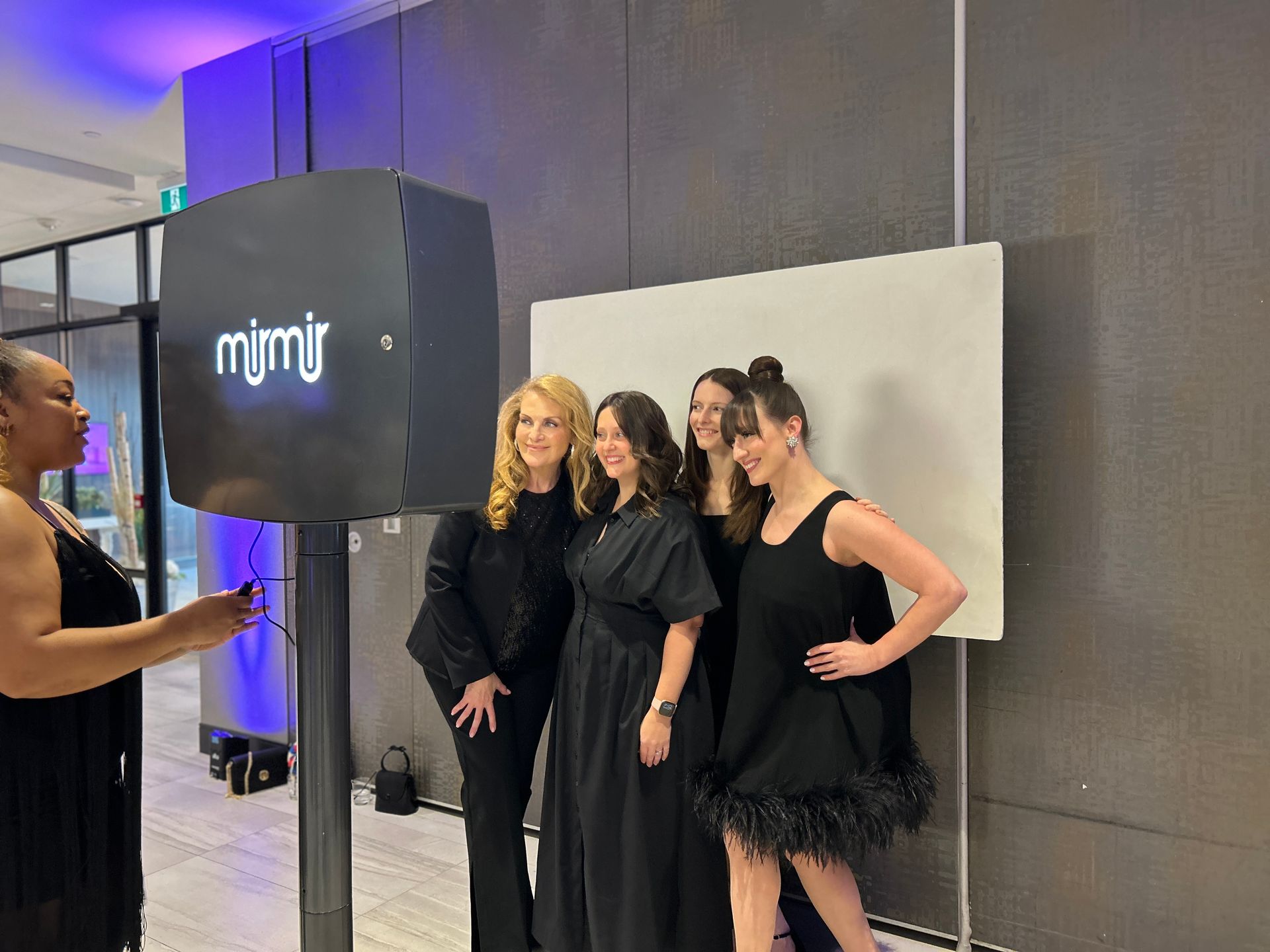 People posing for a photo at an event, near a photo booth, all wearing black outfits.